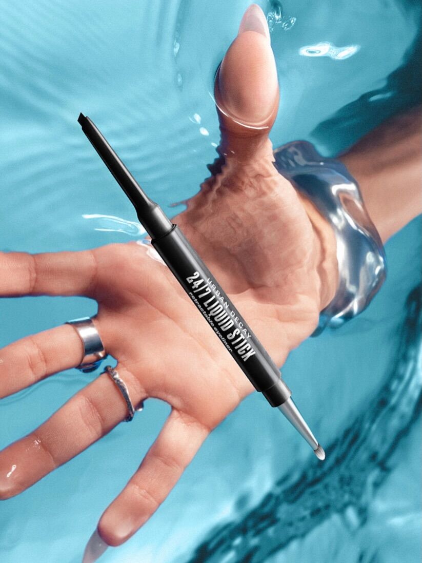 A hand reaching for an urban decay brand liner submirged in water